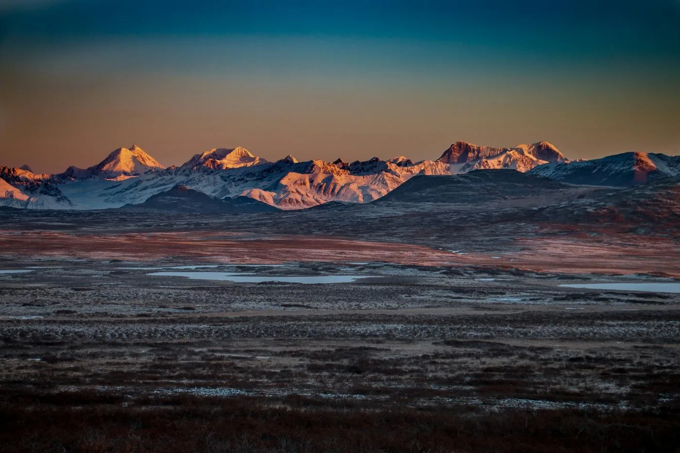 Snow-capped mountain range across autumn tundra at golden hour, Alaska