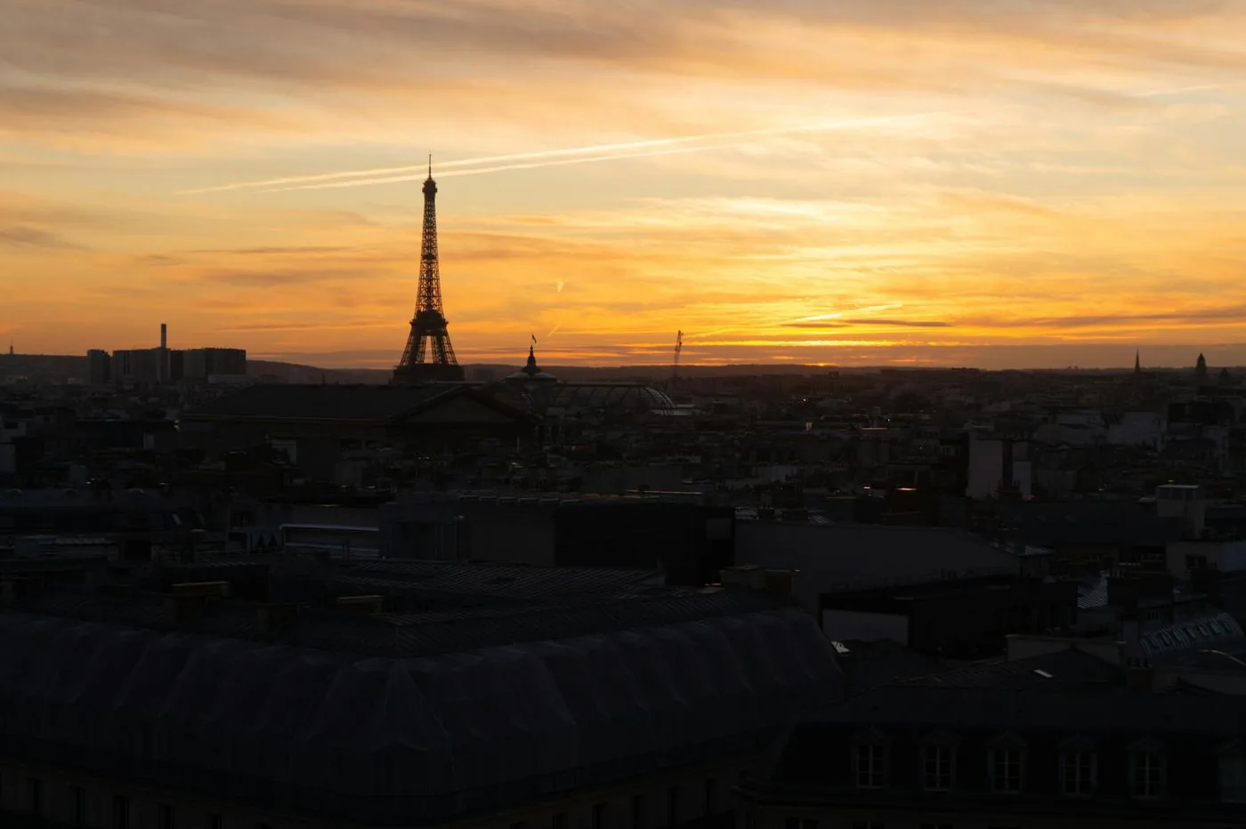 The Eiffel Tower stands in silhouette over Paris rooftops at sunset.