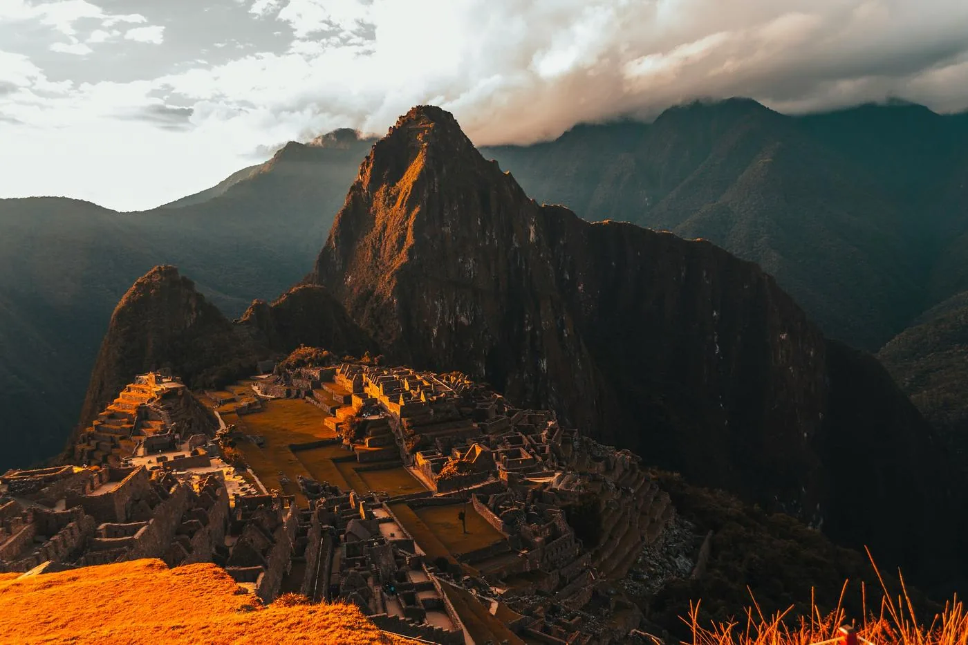Machu Picchu's stone terraces sit beneath a steep, shadowed peak in warm light.