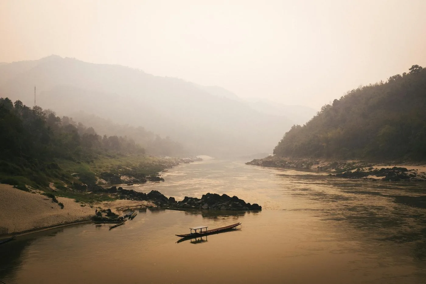 Morning mist over the Mekong River, a longtail boat moored below forested hills