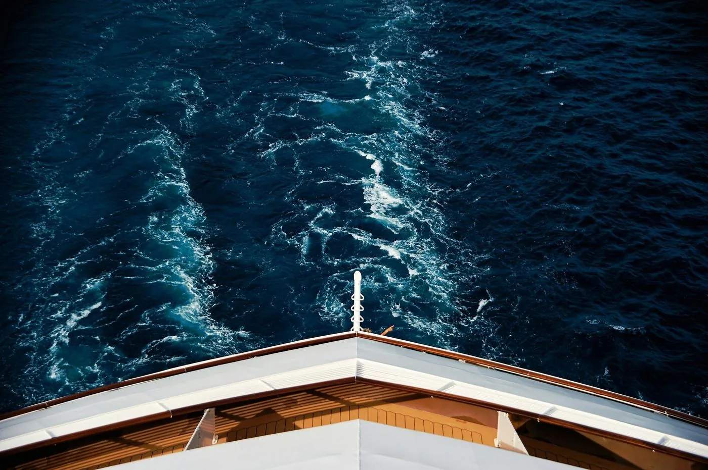 A churning white wake in deep blue water, seen from the upper deck of an ocean liner.